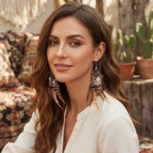 Load image into Gallery viewer, Handmade statement feather earrings worn by a model in outdoor setting