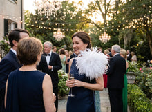 Load image into Gallery viewer, A lady wearing a white ostrich feather brooch on a classic navy suit lapel at a wedding.