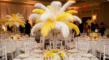 Load image into Gallery viewer, Decorative table centerpieces with yellow and white feathers in a banquet hall.