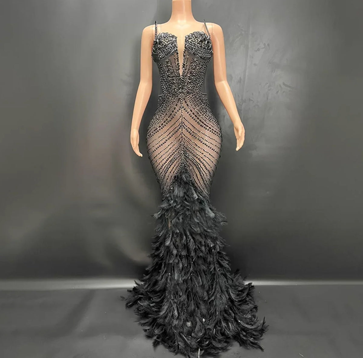 Black beaded evening gown with feathered skirt on a mannequin against a dark background