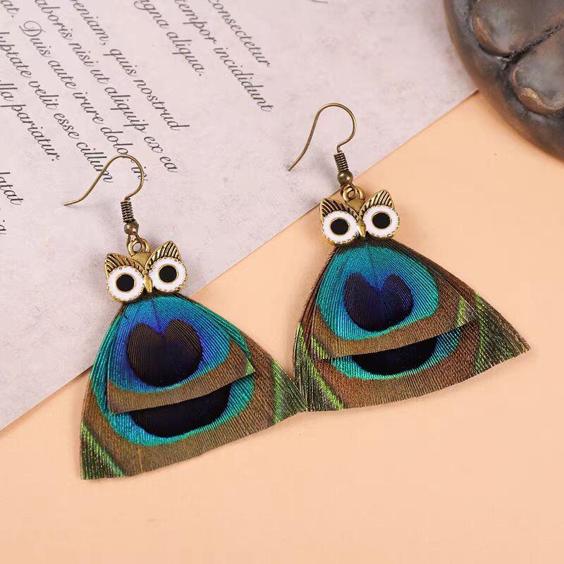 Peacock feather earrings with owl-shaped studs and iridescent blue-green plumage.