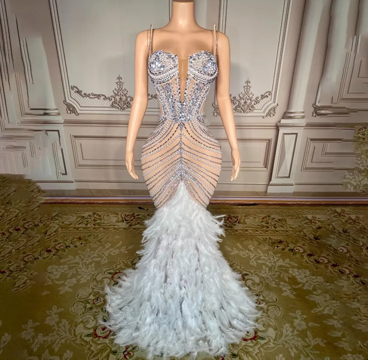 Elegant evening gown with feathered skirt on a mannequin against a decorative wall.