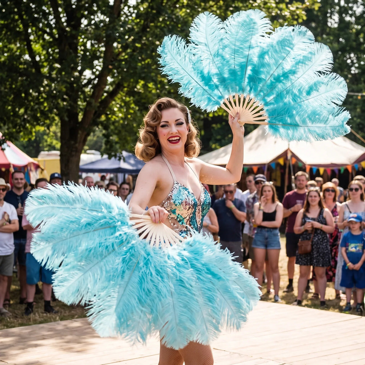 Burlesque dancer performing with light blue ostrich feather fans on an outdoor stage.