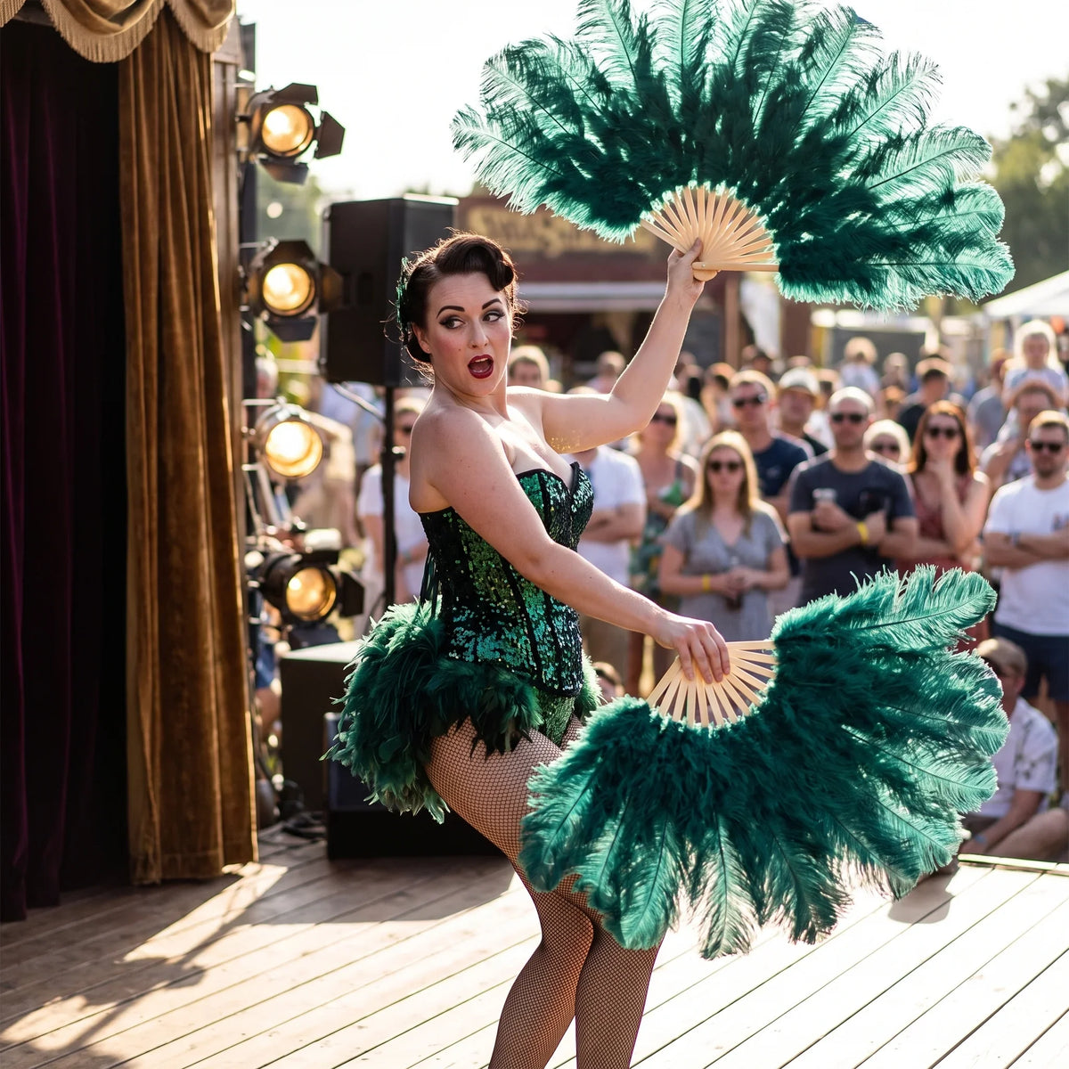 Burlesque dancer in a green sequin corset holding two emerald ostrich feather fans on stage.