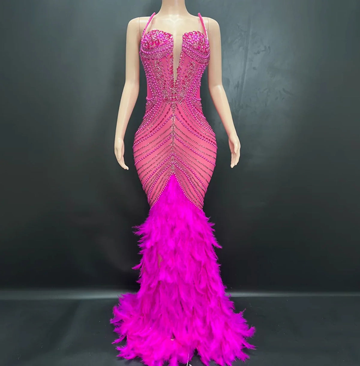 Pink beaded and feathered evening gown on a mannequin against a dark background