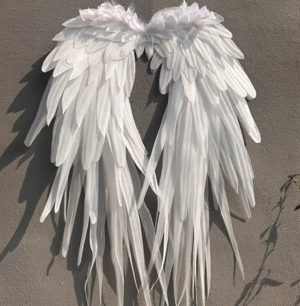 Large white feathered angel wings for dance performance or costume on a grey wall
