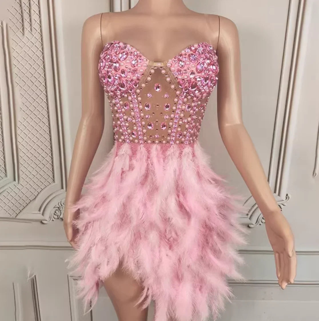 Pink beaded and feathered dress on a mannequin against a decorative wall.