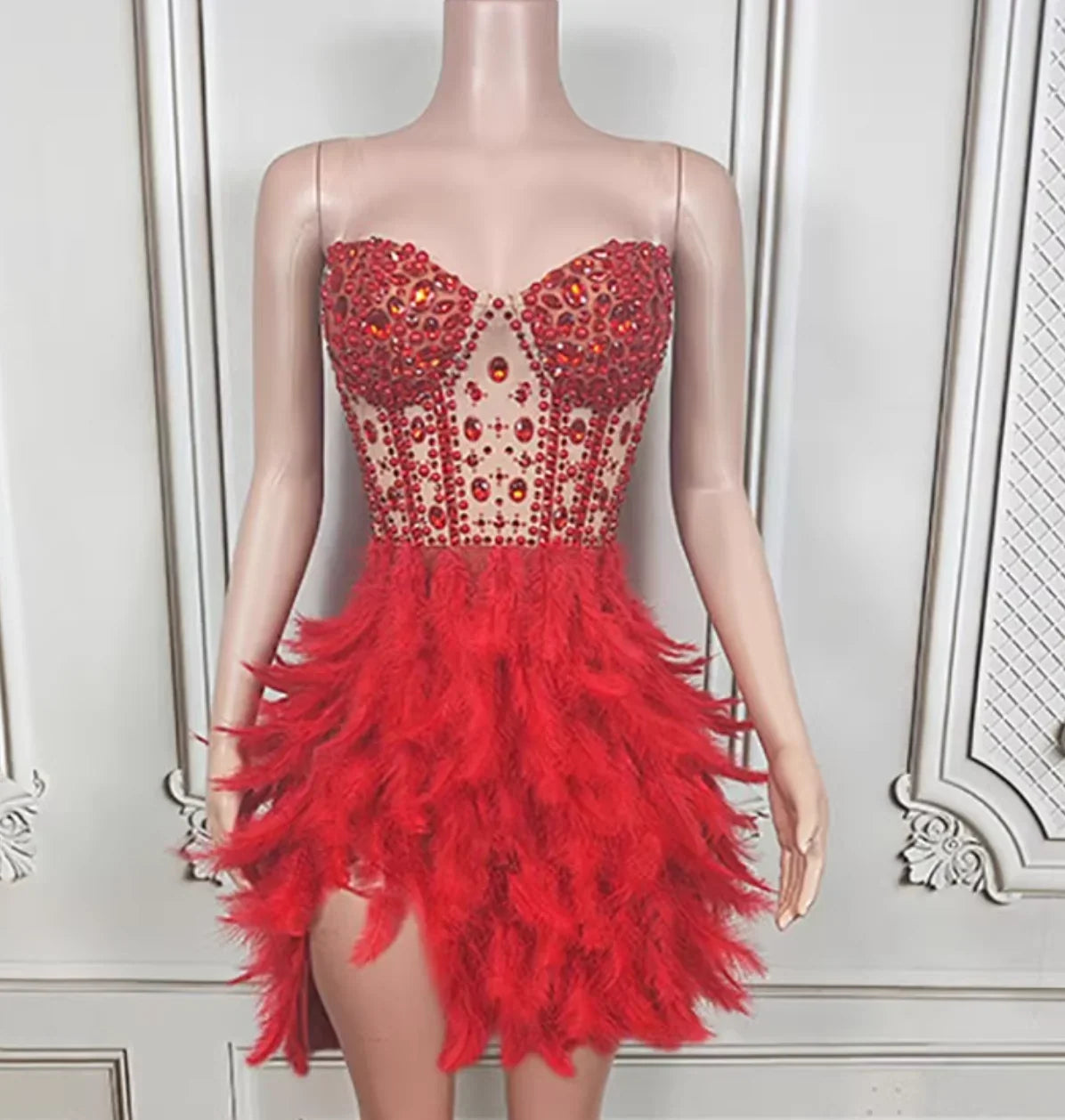 Red dress with feathered skirt on a mannequin against a white wall.