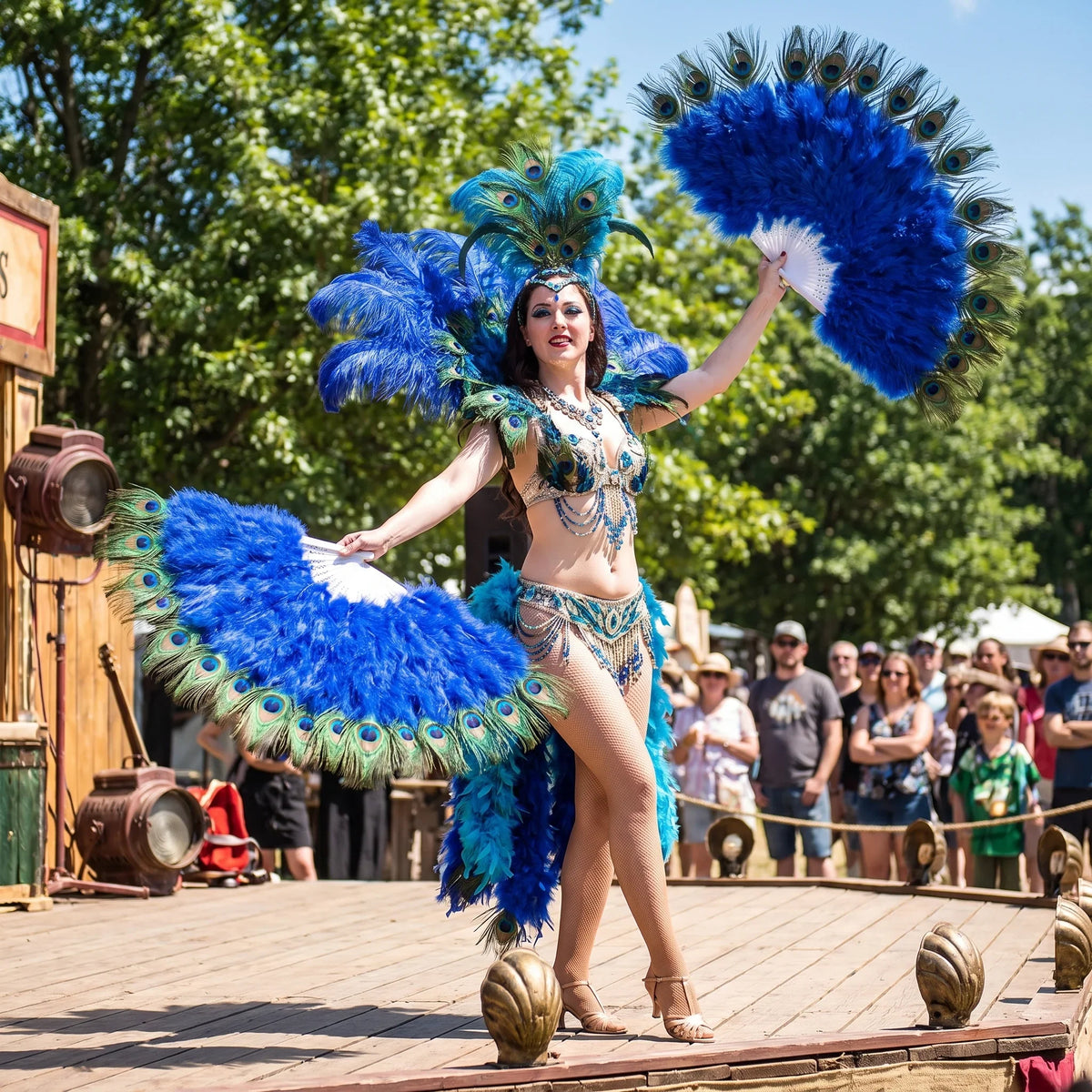 Performer in a blue peacock feather costume holding large blue ostrich feather fans.