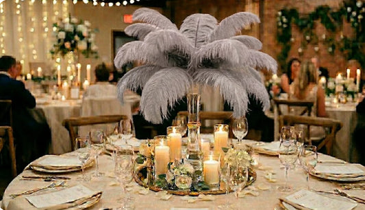 A luxurious silver ostrich feather centerpiece is displayed on a round wedding reception table, surrounded by warm pillar candles and formal place settings.