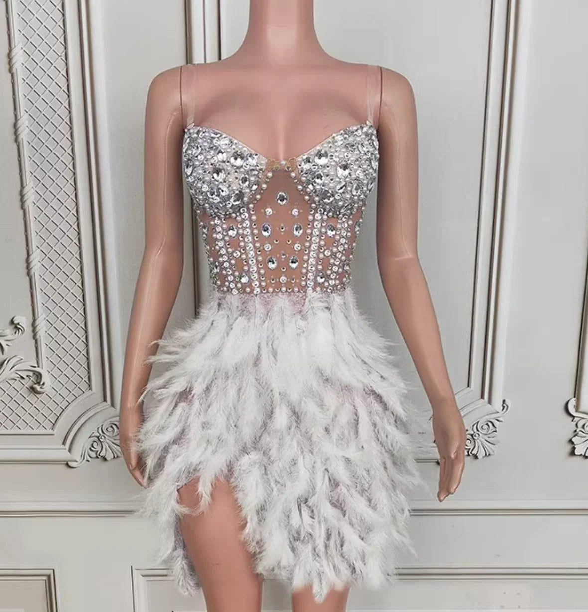 Mannequin wearing a silver sequin and feather dress against a decorative wall.